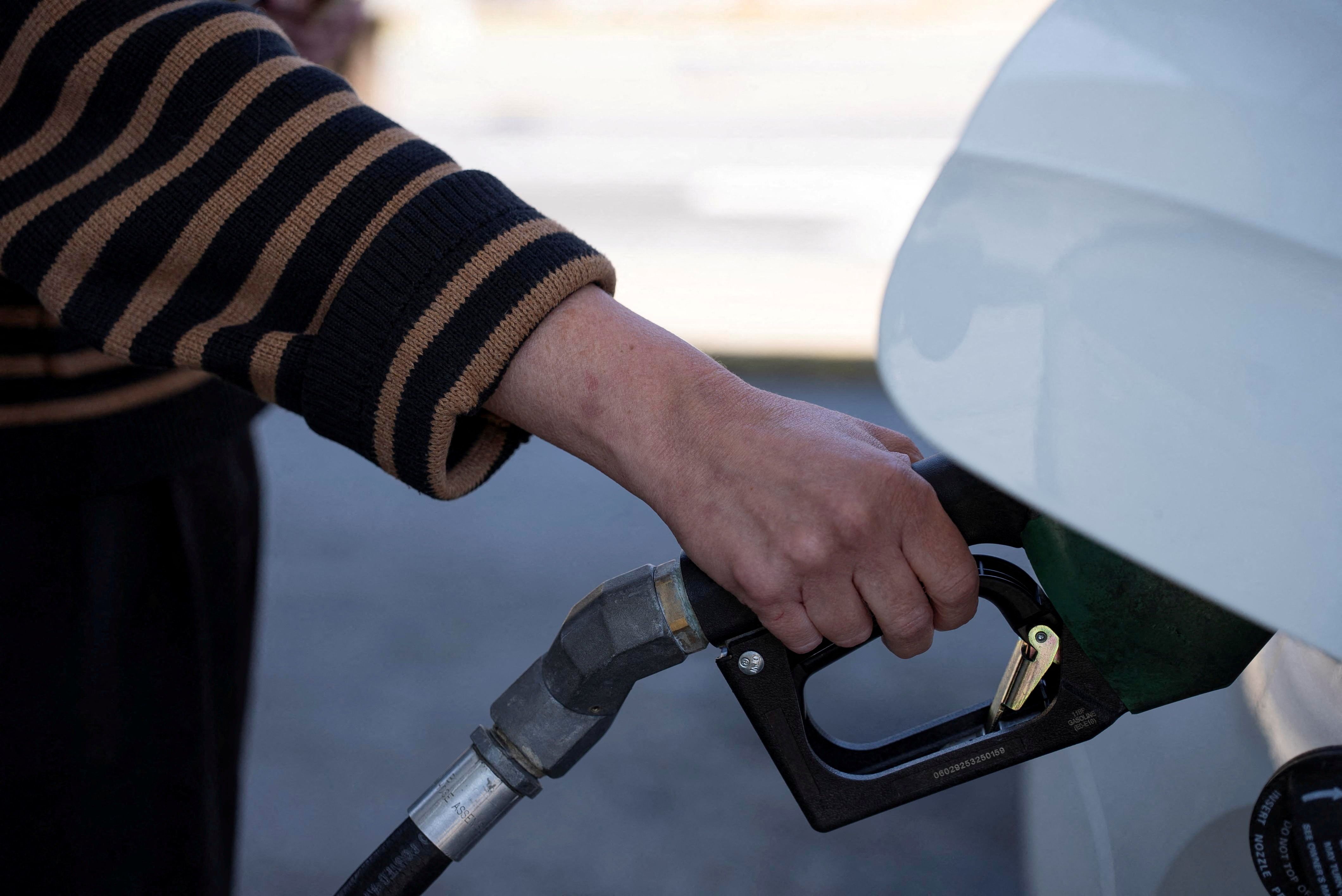 A person pumps gasoline into their car at a gas station. 